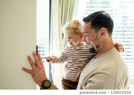 Father showing smart home control to toddler while managing exterior shading system. Father showing smart home control to toddler while managing exterior shading system. 139933836