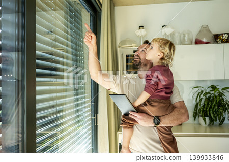 Father showing smart home control to toddler while managing exterior shading system. Father showing smart home control to toddler while managing exterior shading system. 139933846