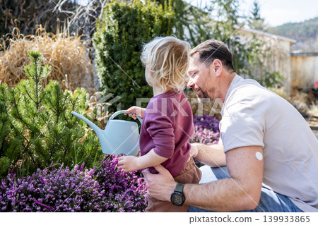 Father and son watering plants together in garden. Father and son watering plants together in garden. 139933865