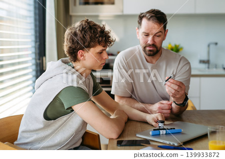 Father checking blood sugar level of diabetic teenage son using glucose meter. 139933872