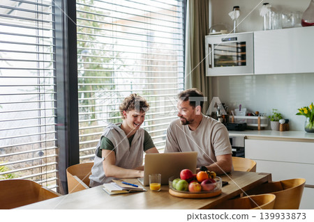 Father helping teenage son with diabetes with homework on laptop in kitchen. Father helping teenage son with diabetes with homework on laptop in kitchen. 139933873