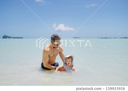 Father and daughter walking in shallow ocean water during beach vacation. Father and daughter walking in shallow ocean water during beach vacation. 139933916