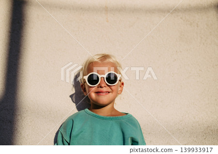 Smiling blond child wearing round sunglasses in warm sunlight. Smiling blond child wearing round sunglasses in warm sunlight. 139933917
