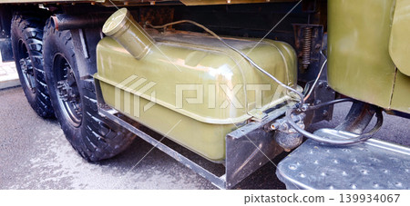 Gas tank of a military truck mounted on the side, featuring a robust design and metallic finish, with large tires and undercarriage visible in the background Gas tank of a military truck mounted on the side, featuring a robust design and metallic finish, with large tires and undercarriage visible in the background 139934067