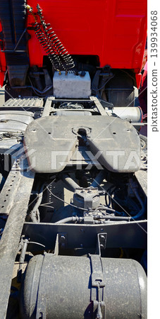 Tractor hitch saddle mounted on a truck chassis, showcasing mechanical components and connections, with a red truck cab visible in the background Tractor hitch saddle mounted on a truck chassis, showcasing mechanical components and connections, with a red truck cab visible in the background 139934068