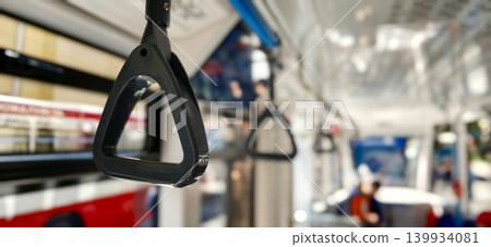 Black handle for holding passengers inside a public bus, with blurred interior elements and seating visible in the background, showcasing urban transportation features 139934081