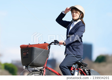 A female office worker riding an electric bicycle while wearing a helmet. A female office worker riding an electric bicycle while wearing a helmet. 139934201
