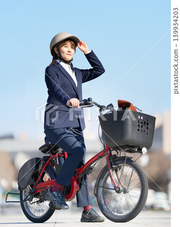 A young woman wearing a helmet commutes to work on an electric bicycle. A young woman wearing a helmet commutes to work on an electric bicycle. 139934203