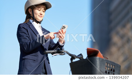 A female office worker using her smartphone while cycling A female office worker using her smartphone while cycling 139934207