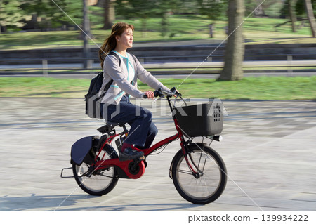 一位身著休閒裝的年輕女子騎著電動自行車穿越城市。 一位身著休閒裝的年輕女子騎著電動自行車穿越城市。 139934222