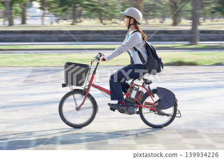 一位年輕女子戴著安全帽騎著電動自行車。 一位年輕女子戴著安全帽騎著電動自行車。 139934226
