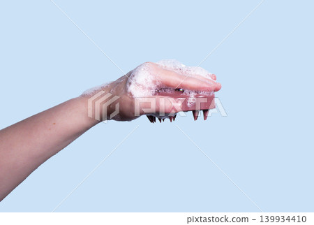 Hair pink scalp massager in woman hand with shampoo foam on blue background isolated. Image with copy space. Mock up for design and banner 139934410