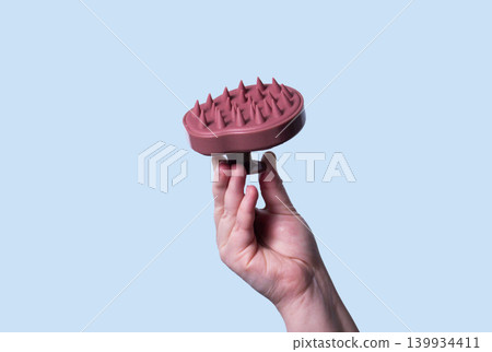 Pink scalp massager brush for hair treatment and care in human hand on blue background 139934411