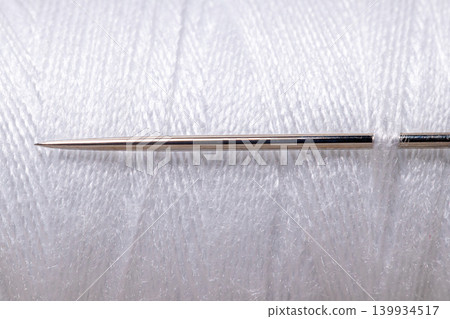 Sharp sewing needle on white thread spool background macro Sharp sewing needle on white thread spool background macro 139934517