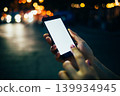 Nighttime hands using phone with glowing city background bokeh blur 139934945