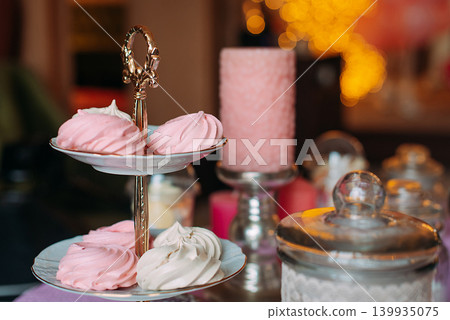 A tiered stand showcases an assortment of pink and white meringues during a gathering. A tiered stand showcases an assortment of pink and white meringues during a gathering. 139935075