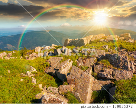 sunset over mountain landscape with stones and grass. view of carpthian mountains in summer. white sharp stones on the rolling hills on top of mountain range under blue sky. weather with rainbow 139935372
