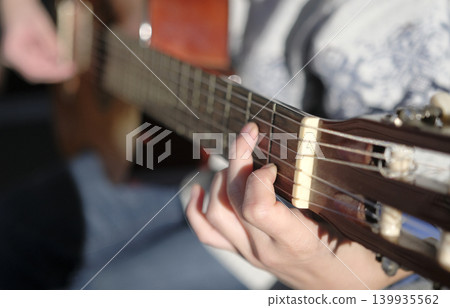 A close-up of a guitarist pinching a chord on a guitar. The musician plays the guitar, focusing on the strings and fingers. Guitar lessons A close-up of a guitarist pinching a chord on a guitar. The musician plays the guitar, focusing on the strings and fingers. Guitar lessons 139935562