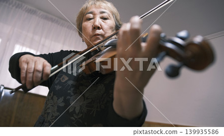 An elderly Asian woman is intently playing the violin, bottom view, focus on the face. An old violinist is learning a new tune. The musician is in a rush of inspiration An elderly Asian woman is intently playing the violin, bottom view, focus on the face. An old violinist is learning a new tune. The musician is in a rush of inspiration 139935586