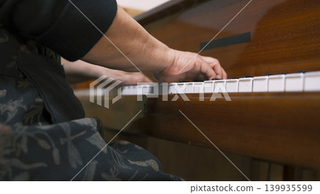 An old man is playing the piano with his hands on the keys. Elderly wrinkled hands of a pianist, close-up, bottom view. A female musician enjoys the music she plays. Piano lessons An old man is playing the piano with his hands on the keys. Elderly wrinkled hands of a pianist, close-up, bottom view. A female musician enjoys the music she plays. Piano lessons 139935599