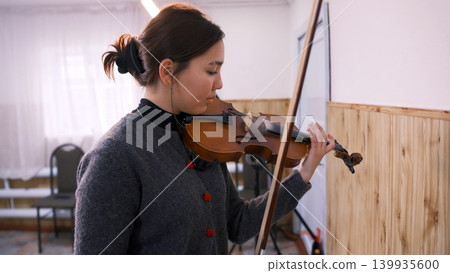 A beautiful young Asian student is learning to play the violin. A young woman plays the violin at a music school. The musician composes a new melody 139935600