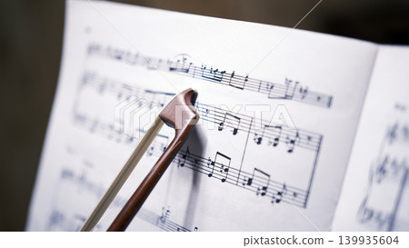 The bow from the violin points to the notes, close-up. A sheet of music with a beautiful melody. Music school. The composer is at work. The concept of music The bow from the violin points to the notes, close-up. A sheet of music with a beautiful melody. Music school. The composer is at work. The concept of music 139935604