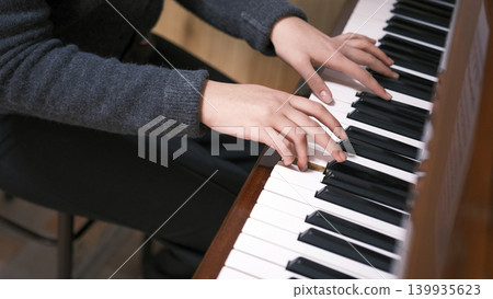 The musician's hands are on the piano keys, close-up. A young woman is playing the piano. The concept of relaxation and enjoyment when the pianist is fully involved in the process The musician's hands are on the piano keys, close-up. A young woman is playing the piano. The concept of relaxation and enjoyment when the pianist is fully involved in the process 139935623