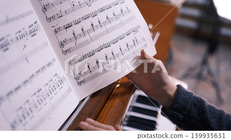 The musician is flipping through a music book, sitting at the piano, close-up. These are the notes of a piano piece, and this person is most likely a pianist or a music student 139935631