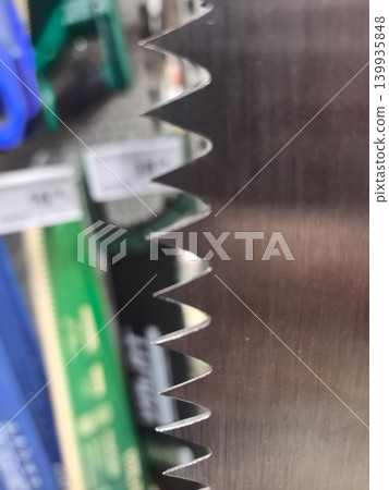 Brightly shining saw blade reveals intricate teeth against blurred backdrop Brightly shining saw blade reveals intricate teeth against blurred backdrop 139935848