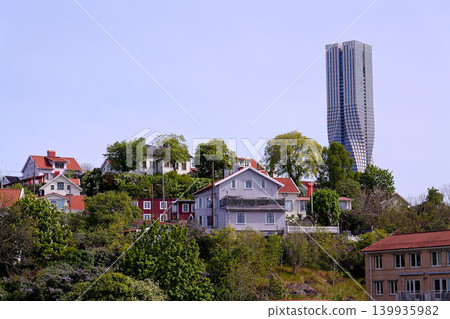 Colony of small wooden historic houses on the Slottsberget mountain with the tallest Scandinavian building Karlatornet skycraper in Lindholmen in background, Gothenburg, Sweden Colony of small wooden historic houses on the Slottsberget mountain with the tallest Scandinavian building Karlatornet skycraper in Lindholmen in background, Gothenburg, Sweden 139935982