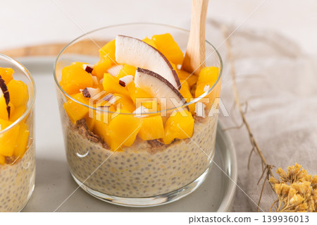 Creamy chia seed pudding layered in a glass topped with vibrant yellow mango cubes and fresh coconut slices served as a healthy breakfast or tropical vegan dessert on a neutral aesthetic background Creamy chia seed pudding layered in a glass topped with vibrant yellow mango cubes and fresh coconut slices served as a healthy breakfast or tropical vegan dessert on a neutral aesthetic background 139936013