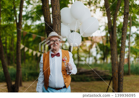 Senior man holding white balloons in park. Senior man holding white balloons in park. 139936095