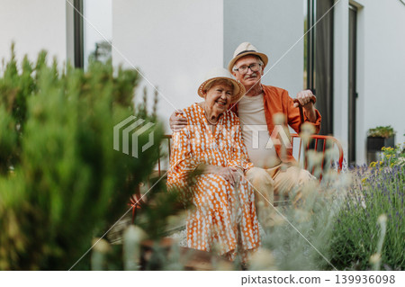 Happy senior couple sitting together in garden bench, smiling and looking at camera. Happy senior couple sitting together in garden bench, smiling and looking at camera. 139936098