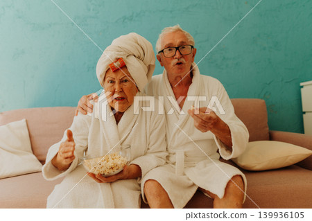 Happy senior couple watching TV and eating popcorn. Happy senior couple watching TV and eating popcorn. 139936105