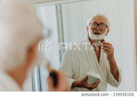 Senior man shaving his beard in the bathroom. Morning routine concept. Senior man shaving his beard in the bathroom. Morning routine concept. 139936108