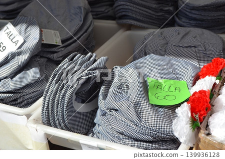 Folded checked caps and traditional garments labeled by size at madrid san isidro market stall for clothing display and retail background Folded checked caps and traditional garments labeled by size at madrid san isidro market stall for clothing display and retail background 139936128