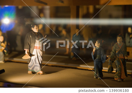 Miniatures depicting scenes of a feudal Japanese city. A sumo wrestler walks on a night street city and some people turn around to look at him. Miniatures depicting scenes of a feudal Japanese city. A sumo wrestler walks on a night street city and some people turn around to look at him. 139936180