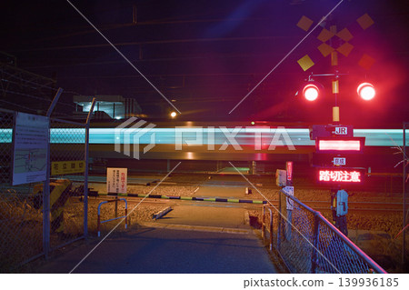 Japanese train crossing in the night. The barrier is closed and the warning red light is on. It seems a train is passing ar high speed due to the long exposure. Japanese train crossing in the night. The barrier is closed and the warning red light is on. It seems a train is passing ar high speed due to the long exposure. 139936185