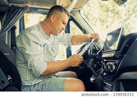 Side view of a male truck driver using a large multimedia touch screen on the dashboard 139936315