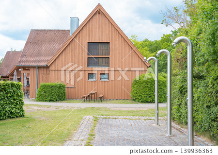 Beautiful view of a traditional wooden building and public steel outdoor showers in a green park zone. Peaceful rural resort landscape on a sunny day Beautiful view of a traditional wooden building and public steel outdoor showers in a green park zone. Peaceful rural resort landscape on a sunny day 139936363