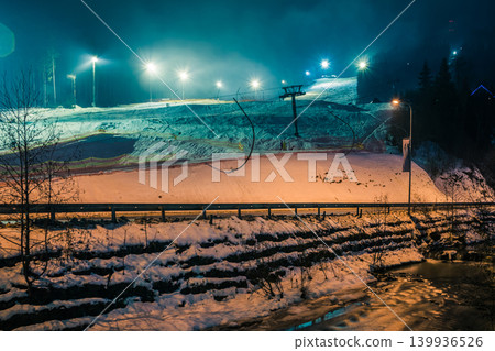 Ski slope illuminated by lanterns at night. A ski resort at night. Lift to climb the mountain. Bukovel. Ukraine Ski slope illuminated by lanterns at night. A ski resort at night. Lift to climb the mountain. Bukovel. Ukraine 139936526