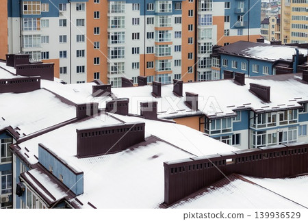 The roof with a chimney is covered with snow in winter. Tall houses in a big city in winter 139936529