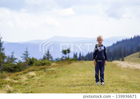 Little boy with a backpack hiking in scenic summer green Carpathian mountains. Child standing alone enjoying landscape mountain view. Active lifestyle, adventure and weekend activity concept. Little boy with a backpack hiking in scenic summer green Carpathian mountains. Child standing alone enjoying landscape mountain view. Active lifestyle, adventure and weekend activity concept. 139936671