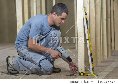 Young professional worker uses level and screwdriver installing wooden frame for future walls. Interior of attic room with oak floor under reconstruction. Renovation and improvement concept. Young professional worker uses level and screwdriver installing wooden frame for future walls. Interior of attic room with oak floor under reconstruction. Renovation and improvement concept. 139936732