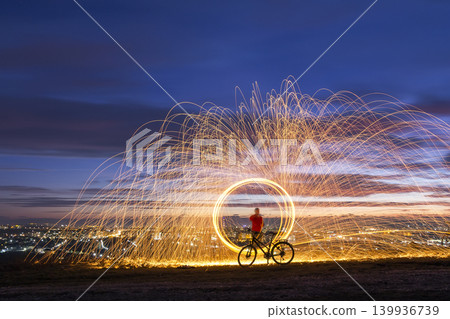 Firework showers of hot glowing sparks from spinning steel wool in night city. Firework showers of hot glowing sparks from spinning steel wool in night city. 139936739