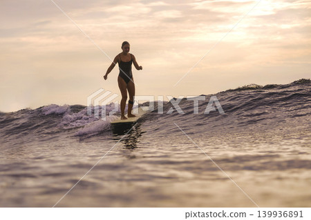 Woman Joyfully Dances Atop Surfboard During Sunset Amidst Gentle Waves Woman Joyfully Dances Atop Surfboard During Sunset Amidst Gentle Waves 139936891