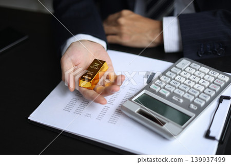 Gold volatility. Businessman calculating profit from fine gold bar investments. 139937499