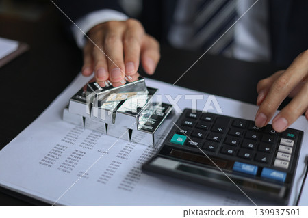 Silver Bullion Investment and Financial Analysis. Businessman Calculating Investment Returns with Silver Bars and Financial Documents. Silver Bullion Investment and Financial Analysis. Businessman Calculating Investment Returns with Silver Bars and Financial Documents. 139937501