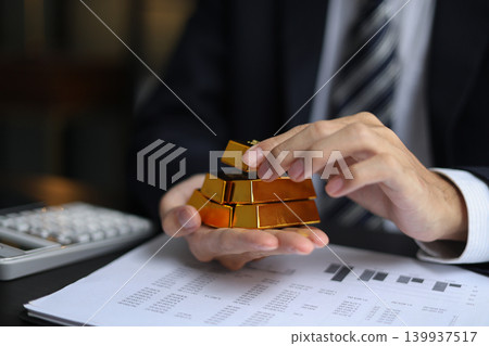 Gold investment. Businessman analyzing financial data with gold bars and calculator on desk 139937517