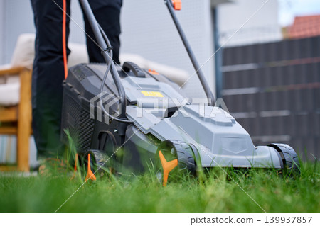 Corded lawn mower on backyard grass with person standing behind Corded lawn mower on backyard grass with person standing behind 139937857